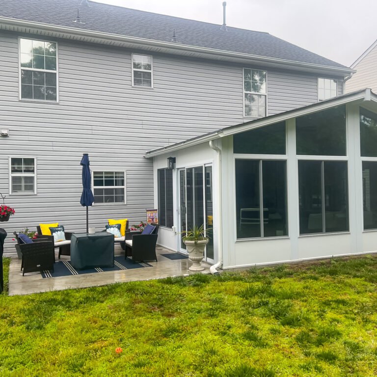 Gable sunroom addition with tall glass panels beside a backyard patio.