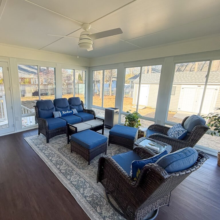 Furnished sunroom with blue seating, large windows, and a ceiling fan.