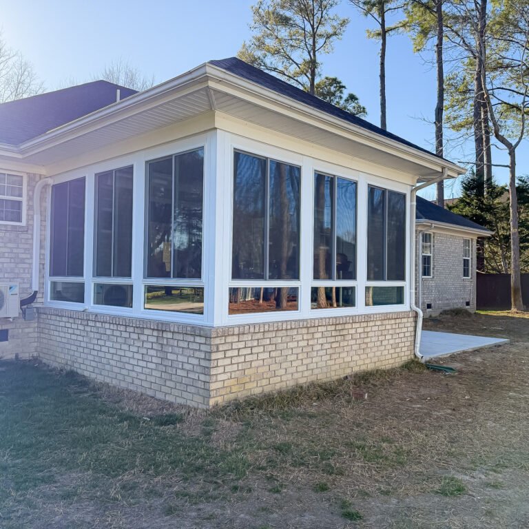 White sunroom addition with large windows, a low-slope roof, and a brick base.