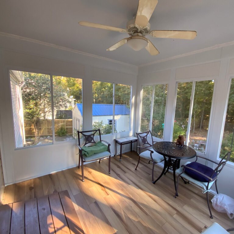 Enclosed sunroom interior with a ceiling fan, seating, and views of the yard.