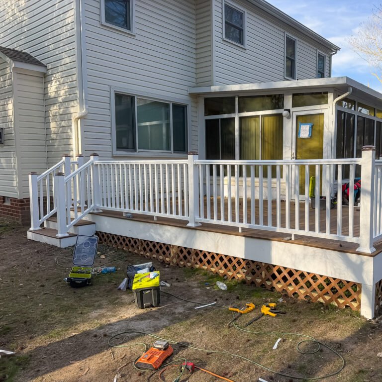 Rear porch enclosure above a deck with white railings and a stairway.